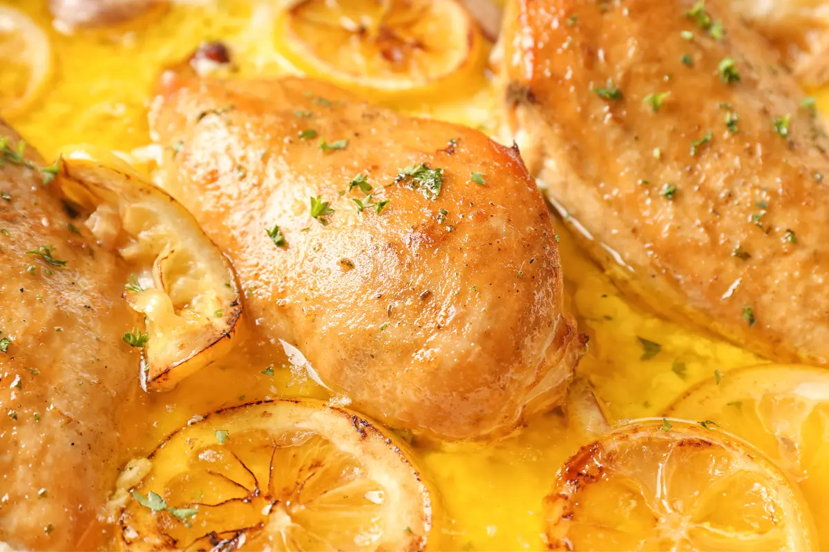 Chicken soaking in a lemon juice marinade with herbs and spices.